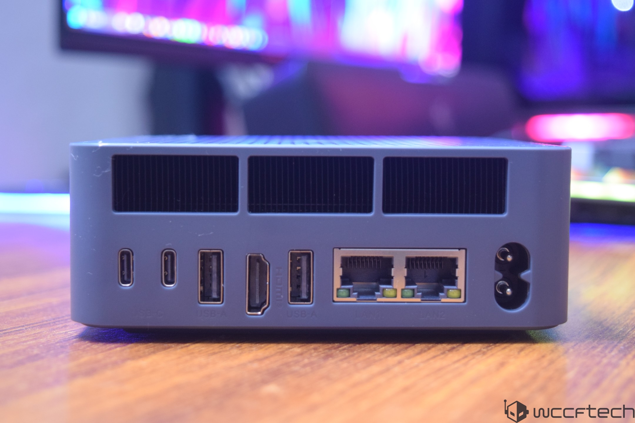 A compact device featuring multiple ports, including two USB-C, two USB-A, one HDMI, and two LAN ports, sits on a wooden surface.