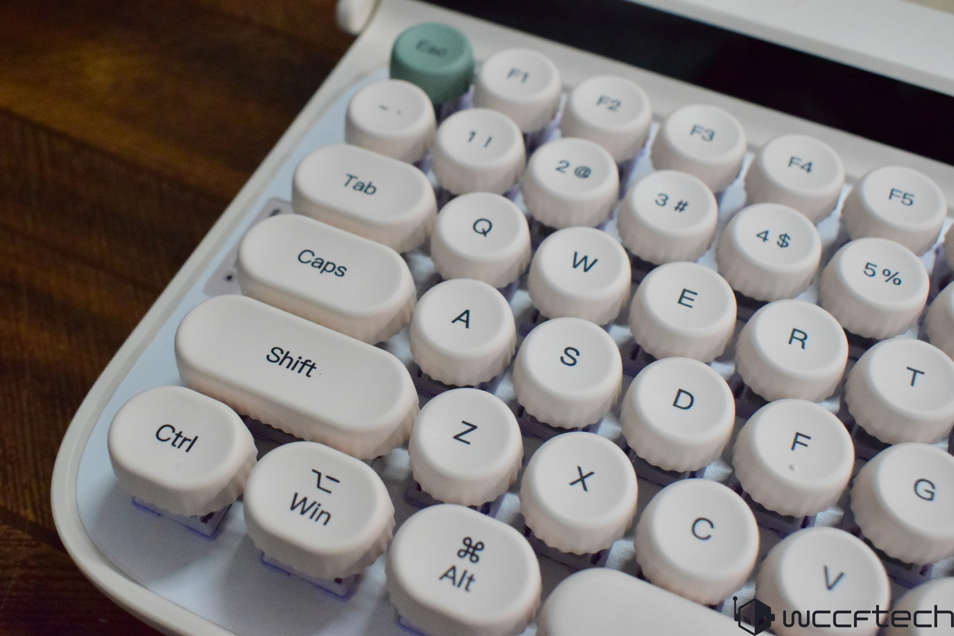 A close-up of a vintage-style mechanical keyboard with round keycaps featuring standard keys like 'Shift,' 'Caps,' and 'Ctrl' on a wooden surface.