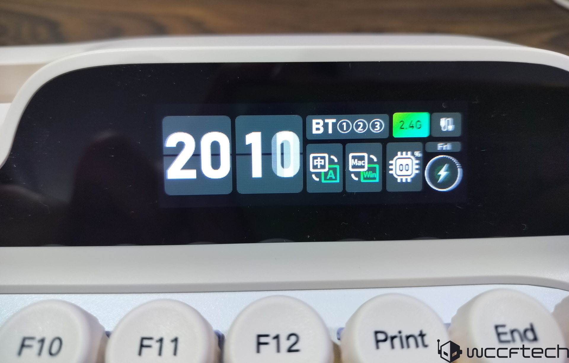 A digital display on a mechanical keyboard shows '2010' with Bluetooth settings and a '2.4G' connection indicator.