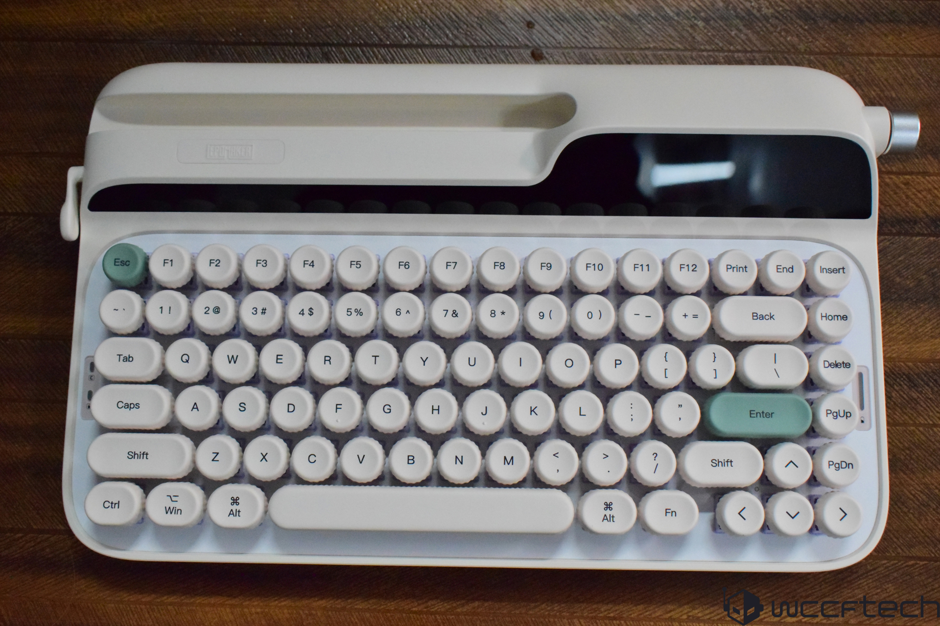 A Qwerkywriter S mechanical keyboard with white round keys and a retro design is displayed on a wooden surface.