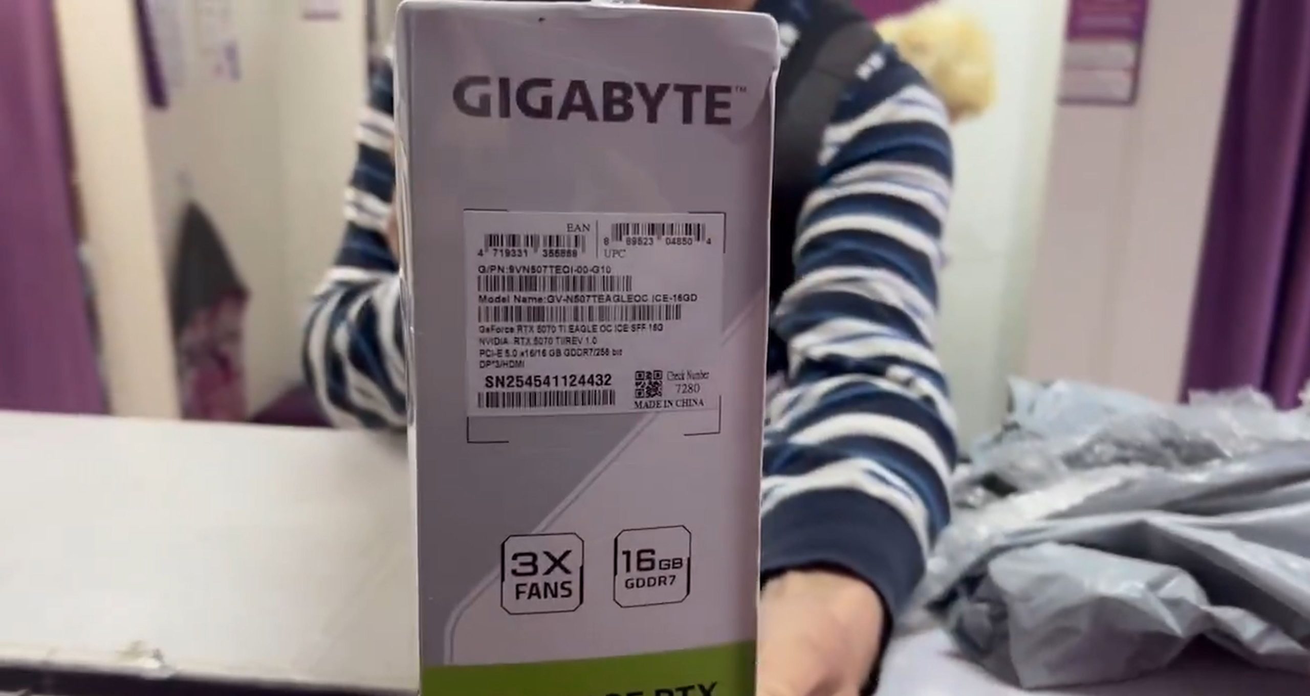 A person holding a Gigabyte GeForce RTX 5070 Ti Eagle graphics card box showing labels with details like '3X FANS' and '16GB GDDR7.'