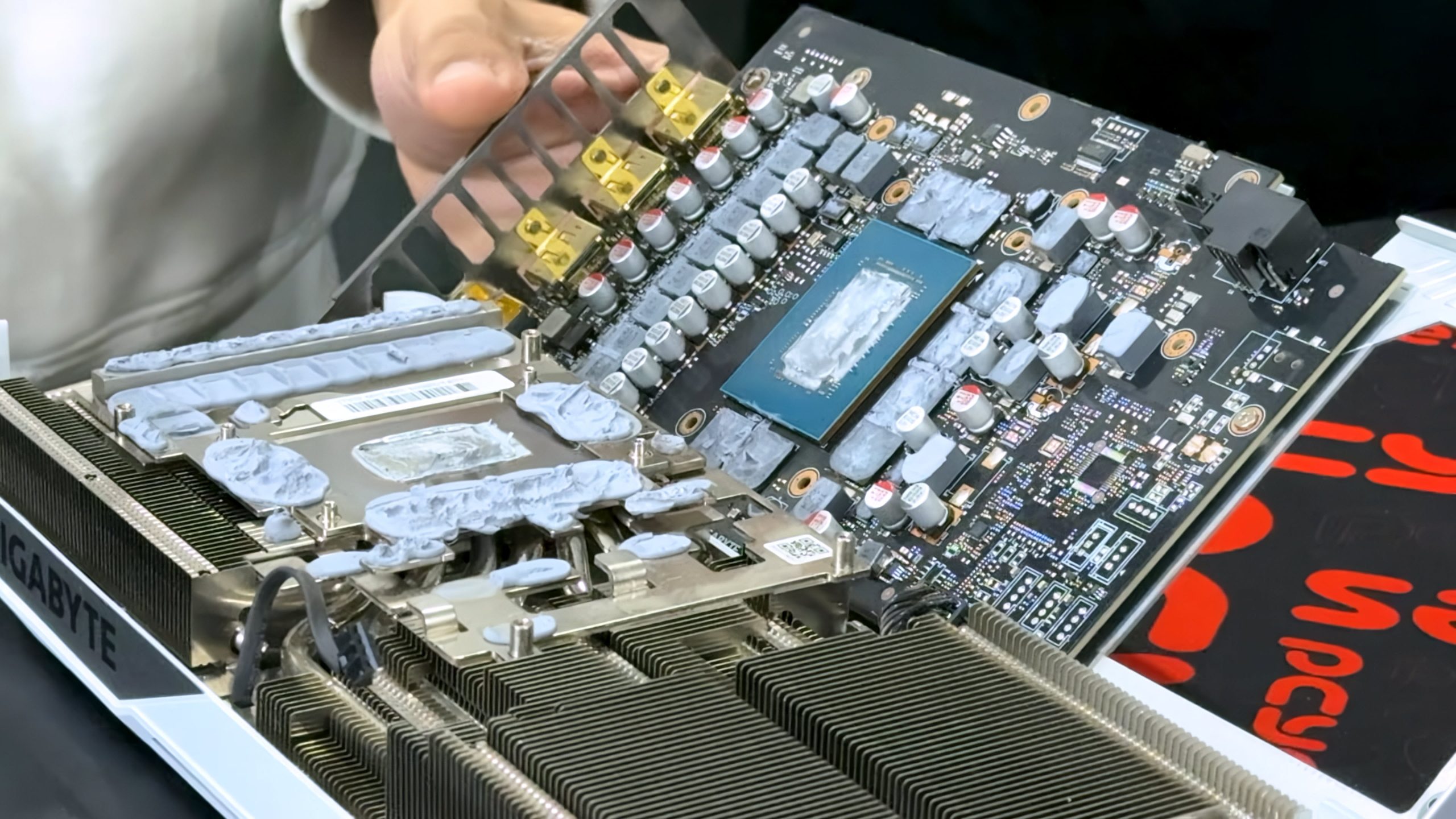 A Gigabyte graphics card is shown with its heatsink removed, revealing the exposed GPU chip and circuitry.