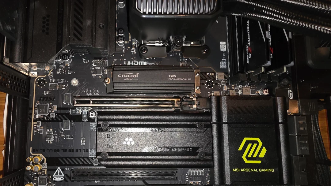 The inside of a PC showcasing a Crucial T700 PCIe Gen5 NVMe M.2 SSD installed on an MSI Arsenal Gaming motherboard.