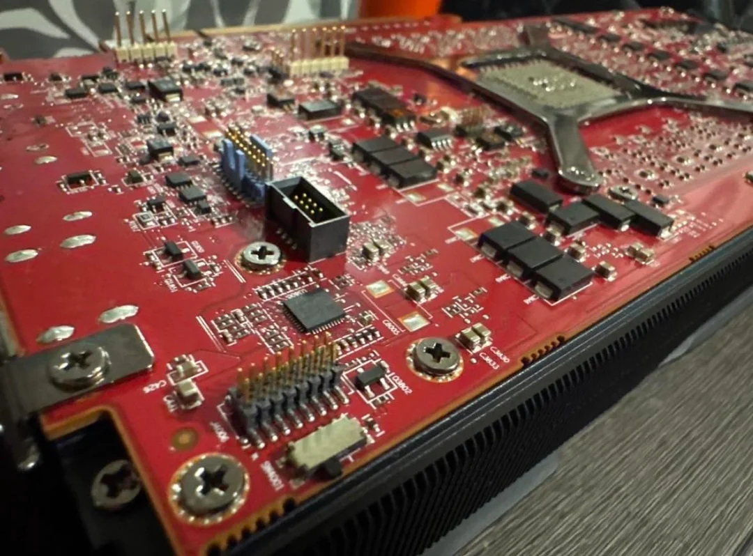 A close-up of the back of an unbranded GPU displaying a red circuit board with various chips, pins, and connectors.