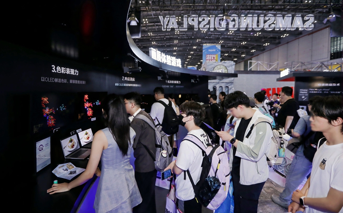 People examining displays at a Samsung booth showcasing OLED technology at a tech exhibition.