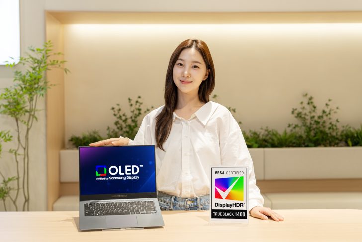 A person is displaying a Samsung laptop showing 'OLED verified by Samsung Display,' alongside a sign for 'VESA Certified DisplayHDR True Black 1400.'