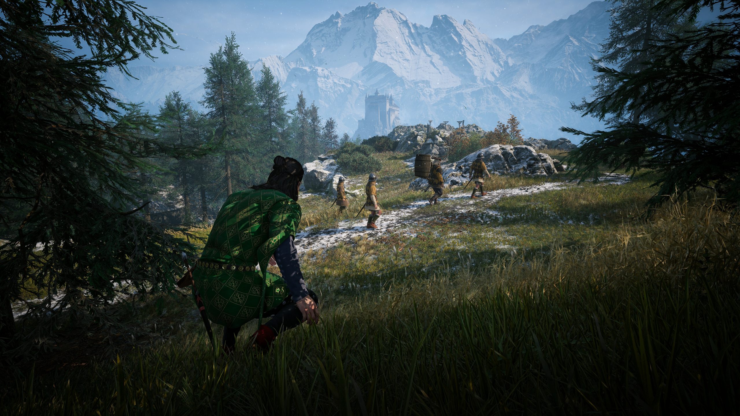 A character in Assassin's Creed Valhalla crouches in the grass observing a group of soldiers walking across a snowy landscape with mountains in the background.