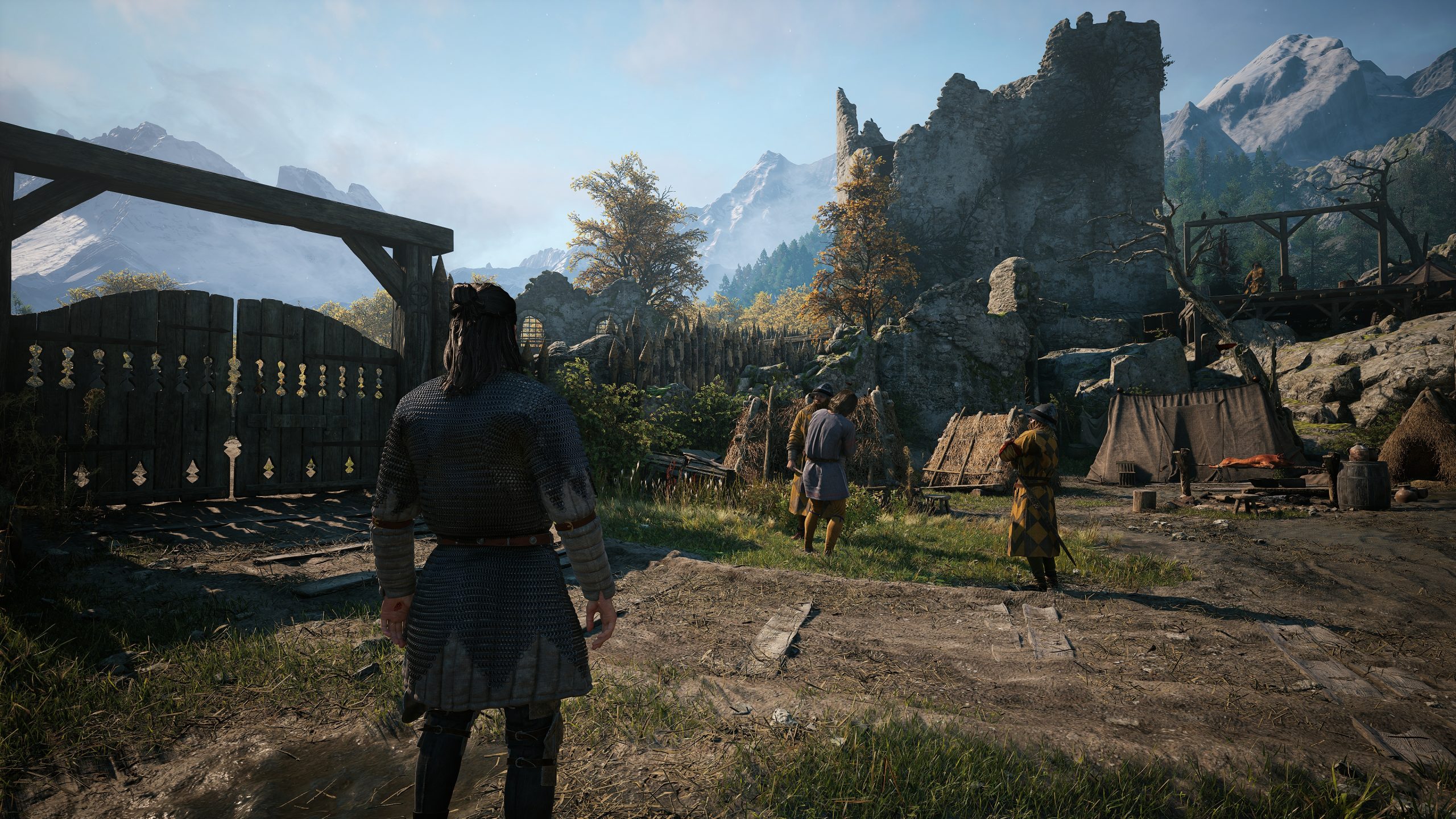 A character from The Witcher game series stands in front of a medieval village scene with ruins and mountains in the background.