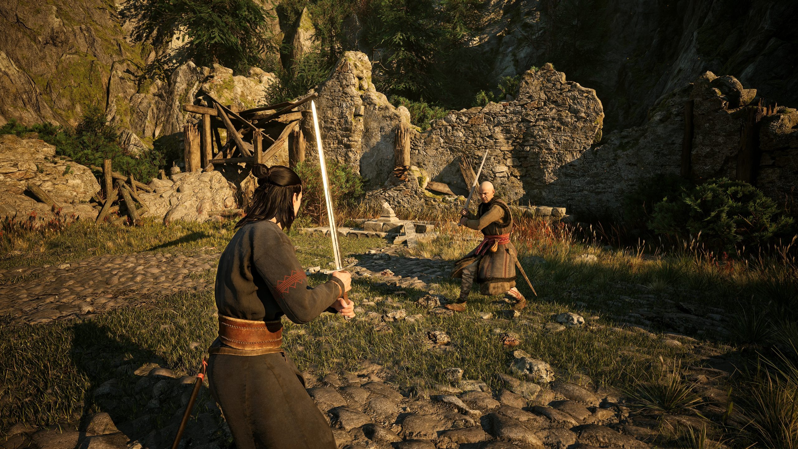 Two characters are engaged in a sword fight in a grassy, stone path setting with ruined stone structures and rocky cliffs, from the game Black Myth: Wukong.