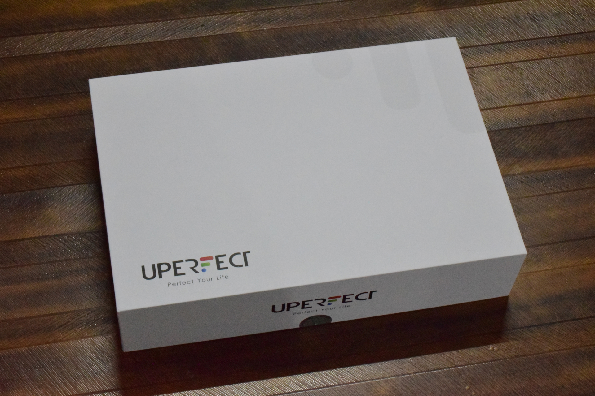 A white box with the UPERFECT logo and the slogan Perfect Your Life on a wooden surface.