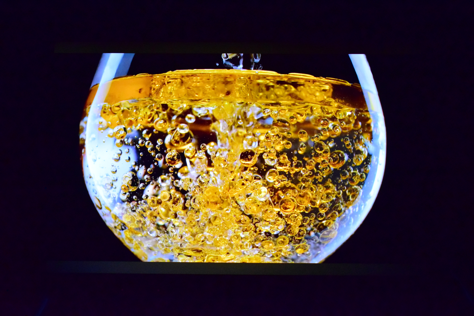 A close-up of bubbles forming in a glass of amber liquid on a dark background.