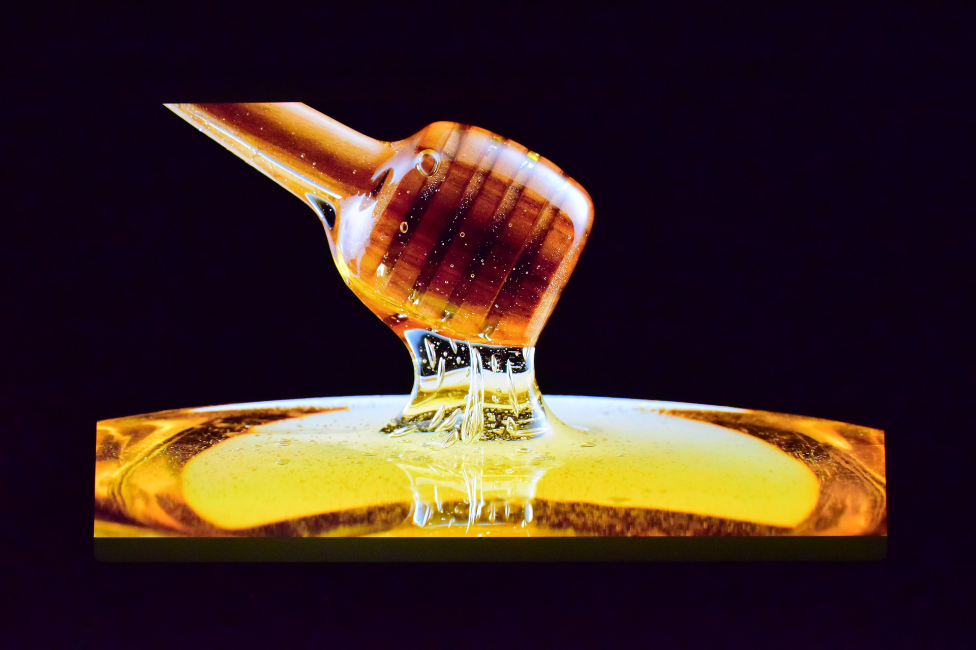 A close-up of golden honey drizzling from a wooden honey dipper against a dark background.