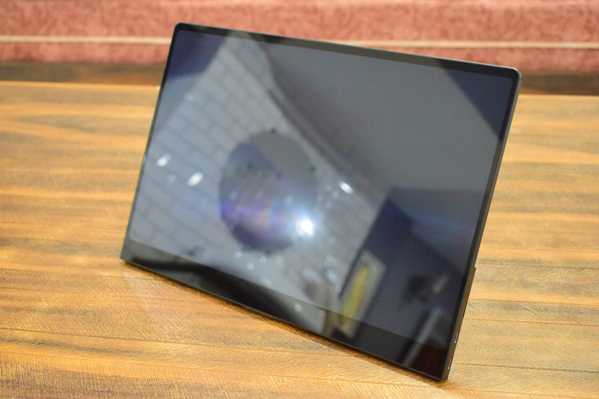 A sleek, unbranded black tablet with a reflective screen is propped at an angle on a wooden surface.