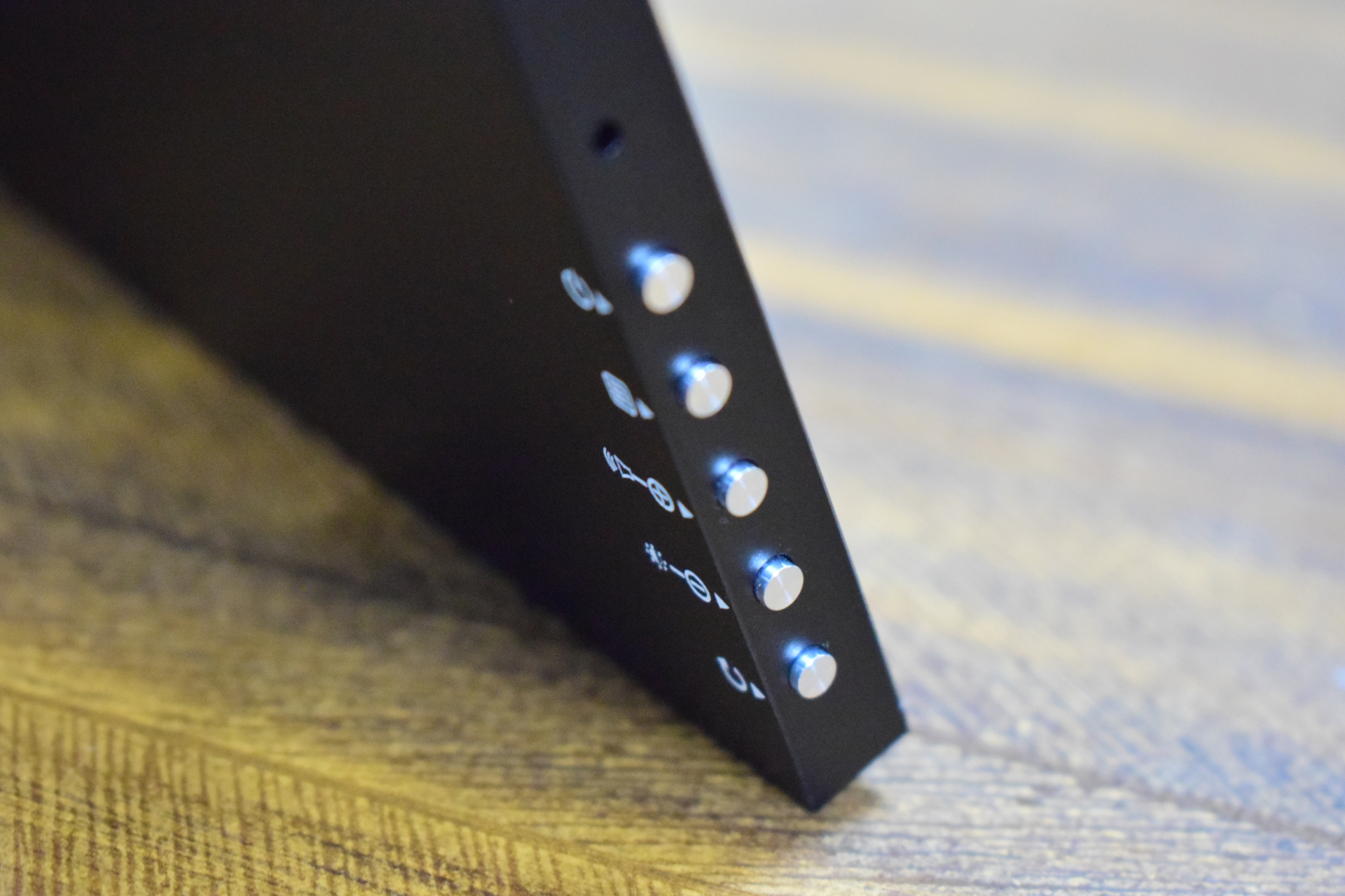 A close-up of an electronic device's side panel featuring four silver buttons and symbols indicating various functions.