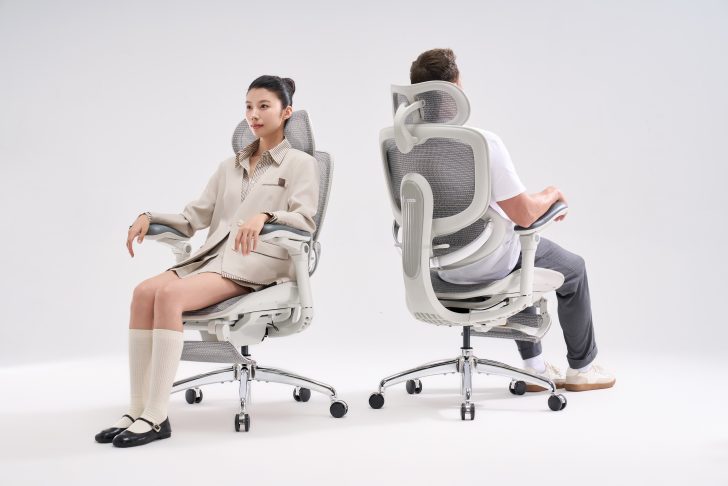 Two people seated back-to-back in sihoo ergonomic office chairs with mesh backrests and adjustable armrests.