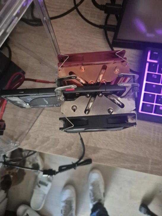 A top-down view of a custom GPU cooler setup on a desk showing a heatsink with copper heat pipes and dual fans next to a partial view of a backlit keyboard.