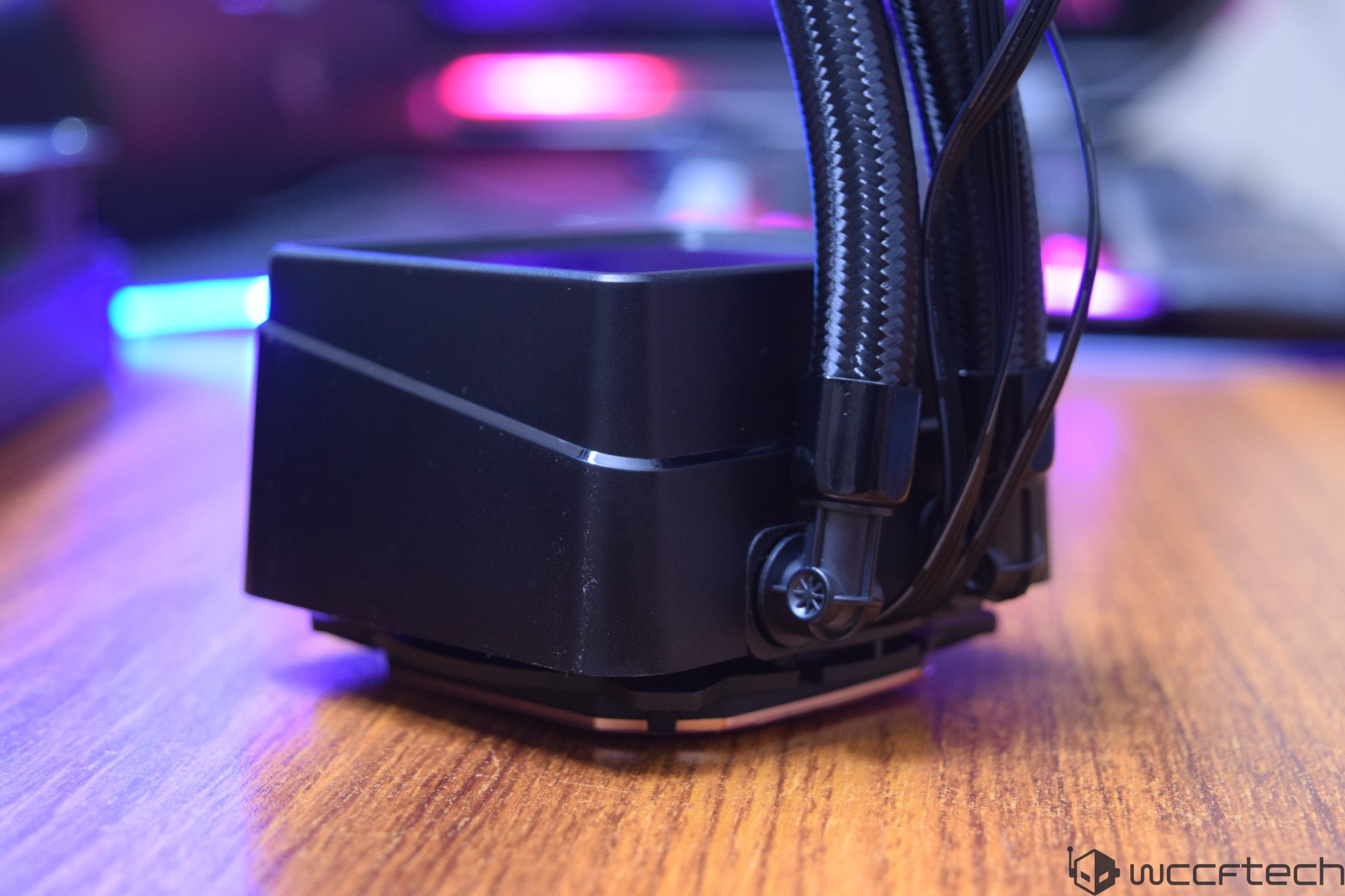 A close-up of a black unbranded liquid CPU cooler on a wooden surface with visible tubing connections.