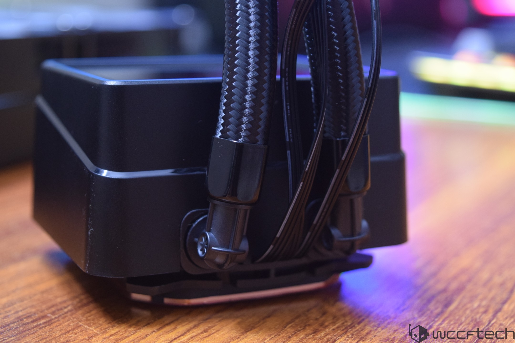 Close-up of an unbranded liquid CPU cooler with a black radiator and braided tubing on a wooden surface.