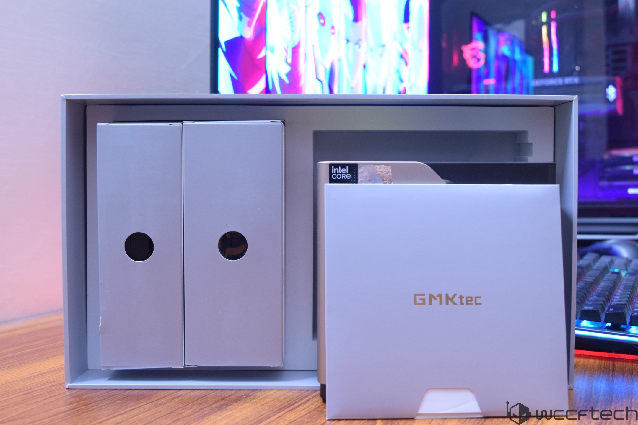 A GMKtec box showing 'Intel Core' branding is displayed in front of a gaming setup with colorful RGB lighting.