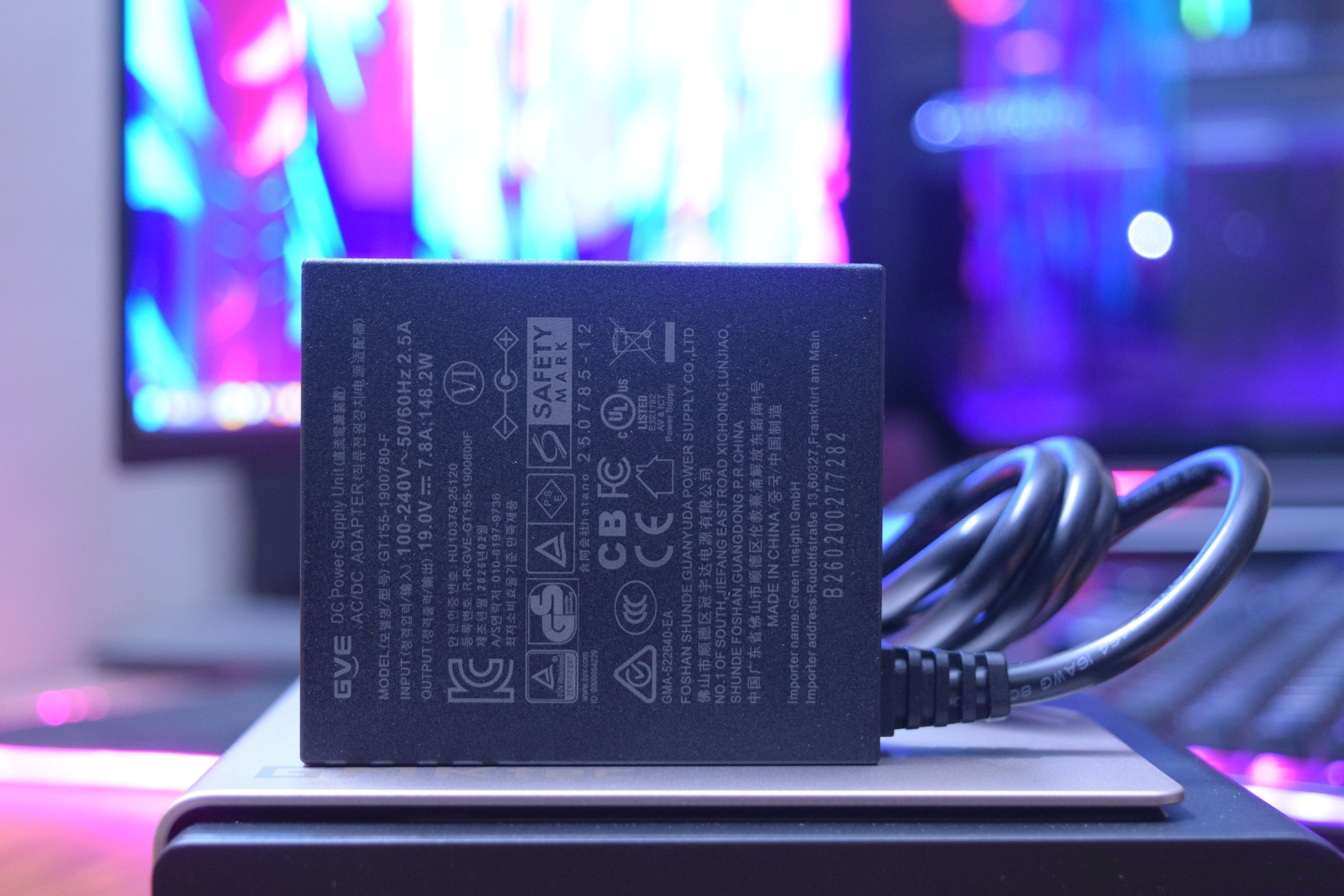 A GVE AC/DC power supply with model number GVE-AD150B-00078 is shown against a colorful computer monitor backdrop.