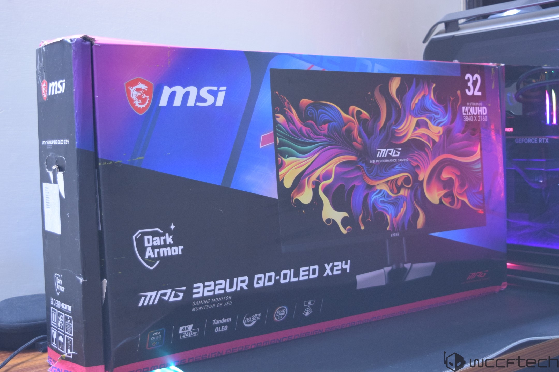 The box for the MSI MPG 322UR QD-OLED X24 gaming monitor is on display next to a computer case with visible GeForce RTX branding.