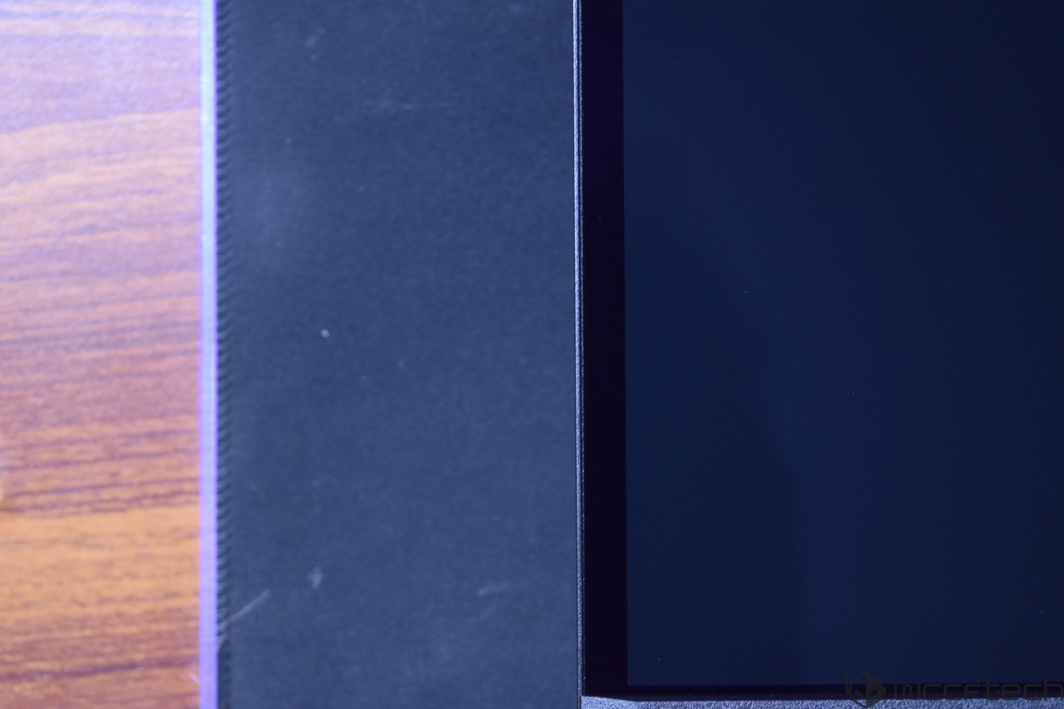The image shows the edge of a black unbranded monitor with a thin bezel on a wooden surface.