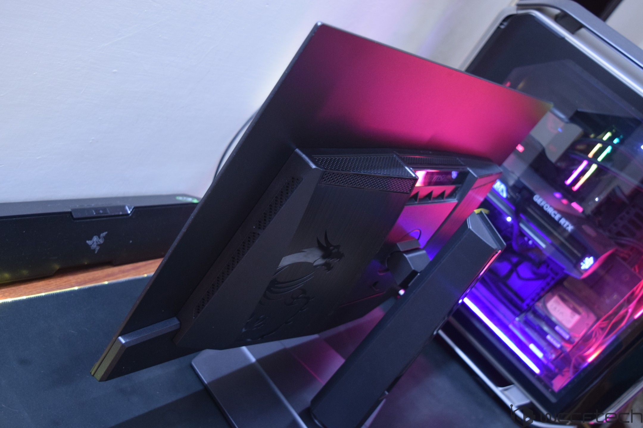 An MSI gaming monitor and a PC case with RGB lighting and a visible GeForce RTX logo are on display beside a Razer soundbar.