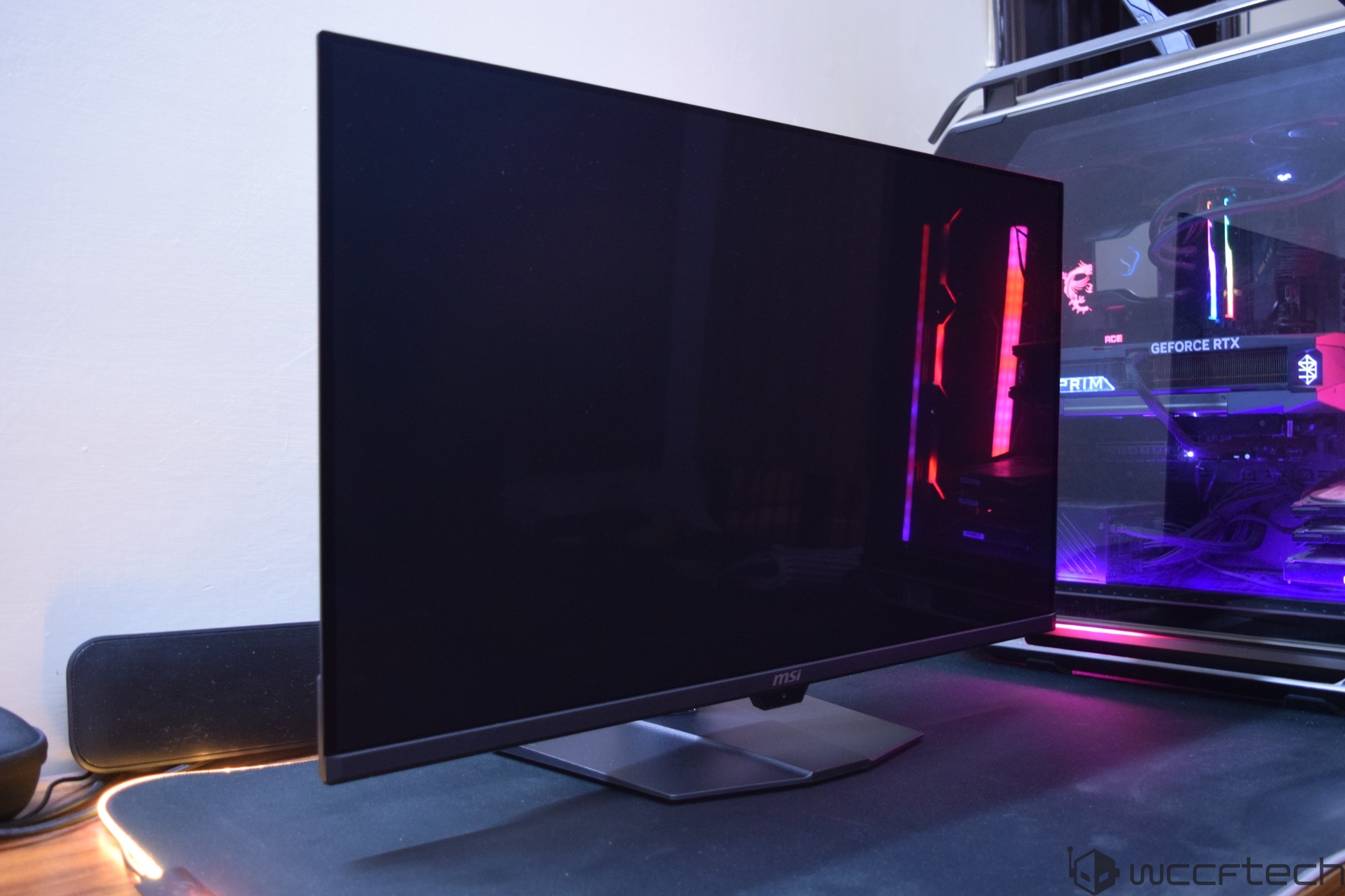 An MSI monitor next to a gaming PC featuring a GeForce RTX graphics card inside a case with colorful RGB lighting.