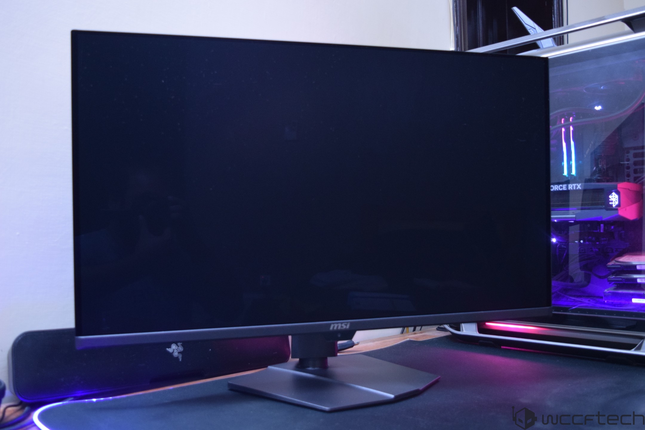 An MSI monitor is set up on a desk next to a gaming PC with visible 'GeForce RTX' branding inside the case.