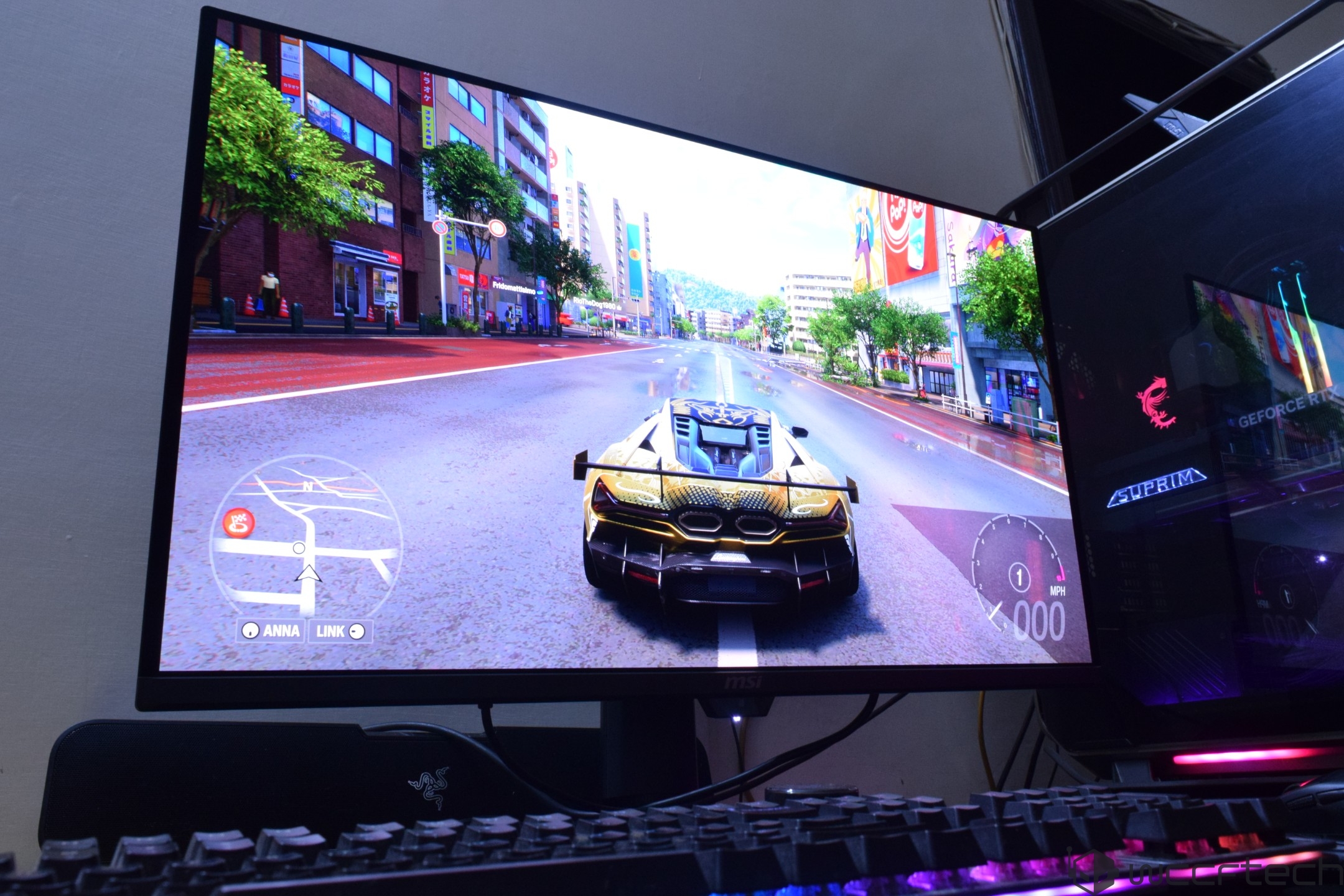 A racing game displayed on an MSI monitor shows a sports car driving on a city street with a mini-map featuring 'ANNA' and 'LINK.'