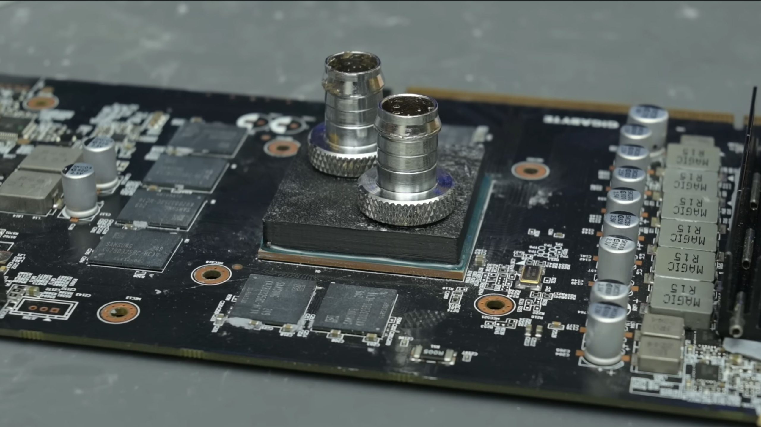 A Gigabyte graphics card is displayed with exposed Samsung memory chips and a custom liquid cooling block installed on the GPU.