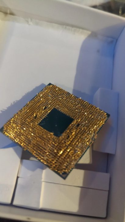A close-up of an unbranded CPU with bent gold pins on a white surface.