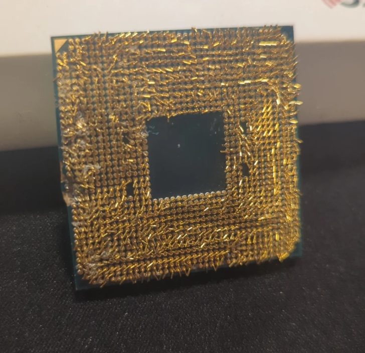 A close-up of a microchip with numerous bent and damaged gold pins on a black surface.