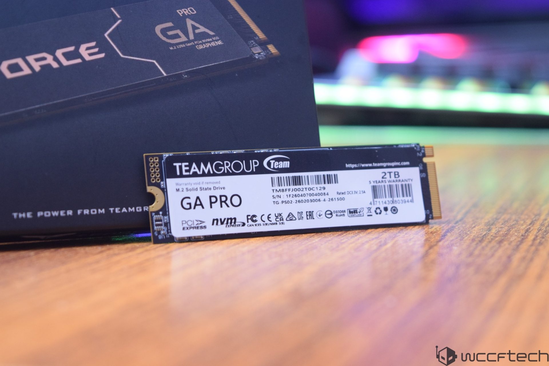 A Teamgroup T-Force GA Pro NVMe 2TB solid state drive is displayed on a wooden surface with its packaging in the background.