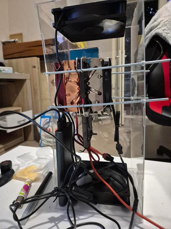A clear acrylic case houses a vertically mounted cooling system with two large fans and various wires attached.