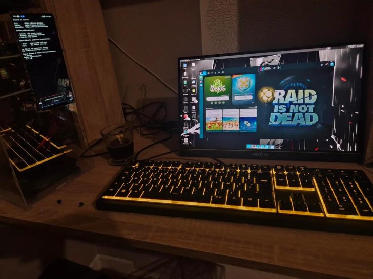 An Arzopa monitor displays a desktop screen featuring the game launcher with the text 'RAID IS NOT DEAD', next to a glowing yellow keyboard on a desk setup.