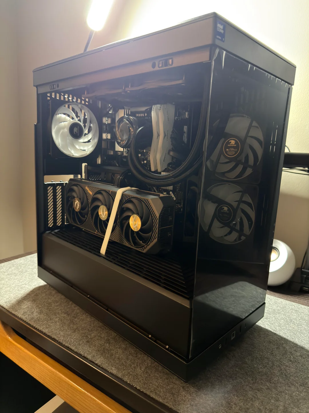 A custom gaming PC case with internal RGB fans, a large graphics card, and a prominent cooling system is displayed on a desk.