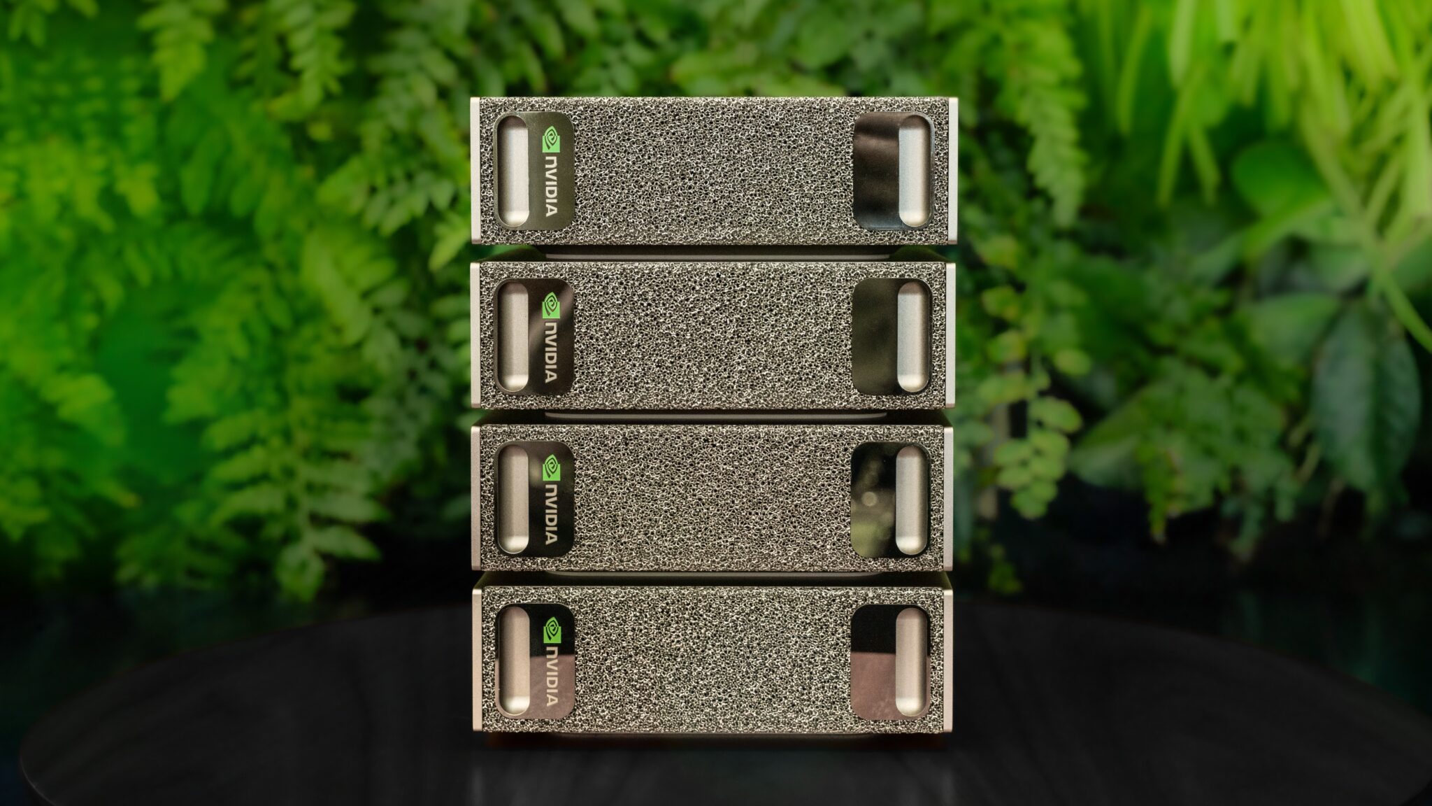 A stack of four Nvidia servers with a textured front panel and the Nvidia logo, set against a green leafy background.