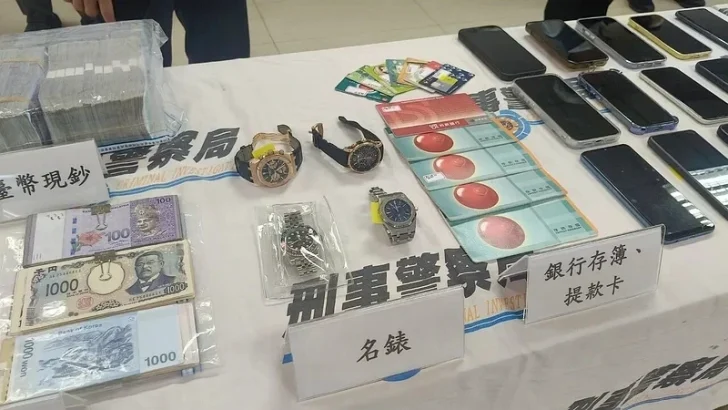 Multiple smartphones, watches, cash, and cards are displayed on a table labeled with Chinese text.